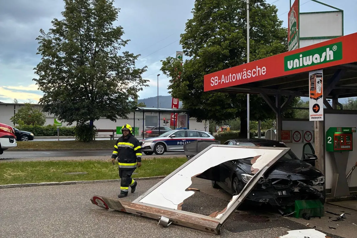 Ein schwarzes Auto mit stark beschädigter Front steht in einer SB-Autowaschanlage. Ein Feuerwehrmann ist ebenfalls im Bild zu sehen.