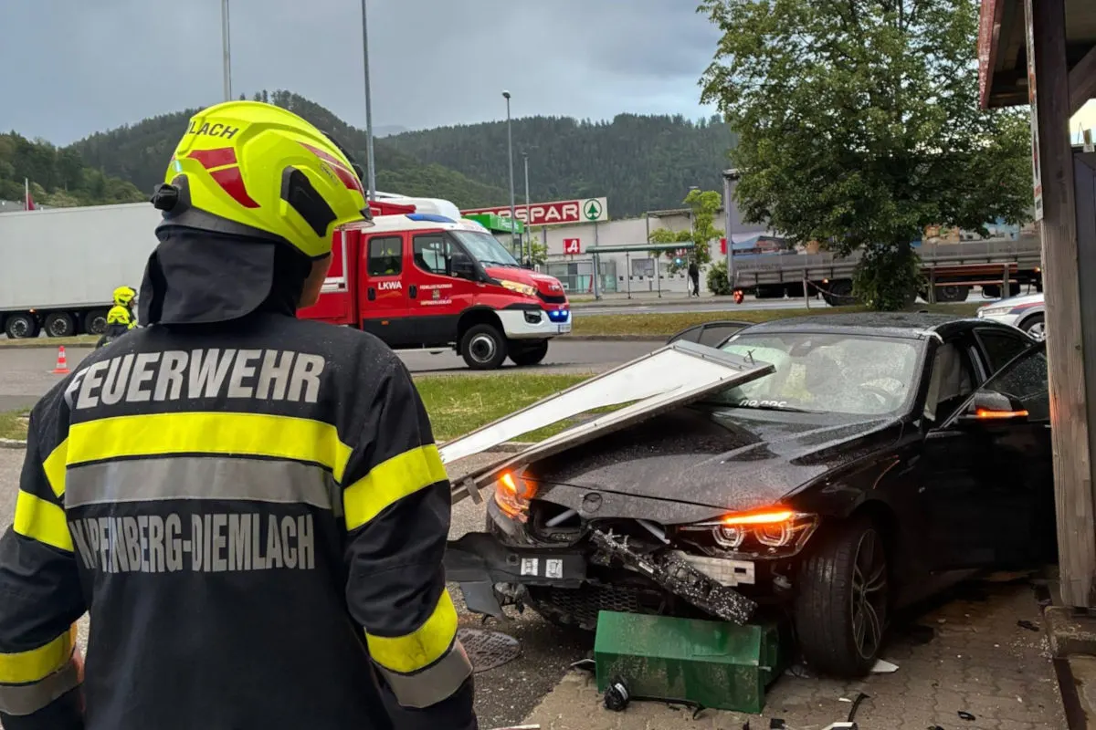 Ein Feuerwehrmann in Schutzkleidung steht vor einem schwarzen Auto, das vorne beschädigt ist. Auf dem Auto liegen herumliegende Trümmer.