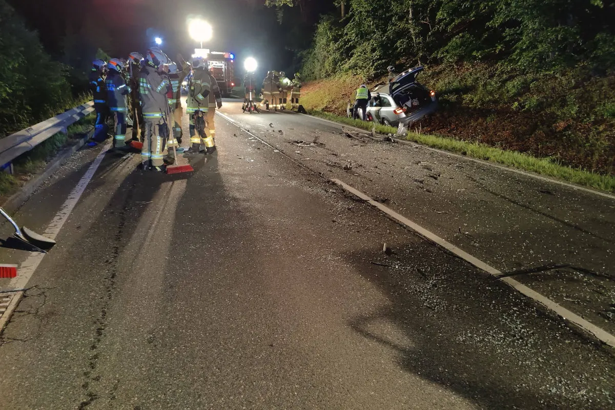 Mehrere Feuerwehrleute stehen auf einer Landstraße bei Nacht. Ein Auto ist von der Fahrbahn abgekommen.