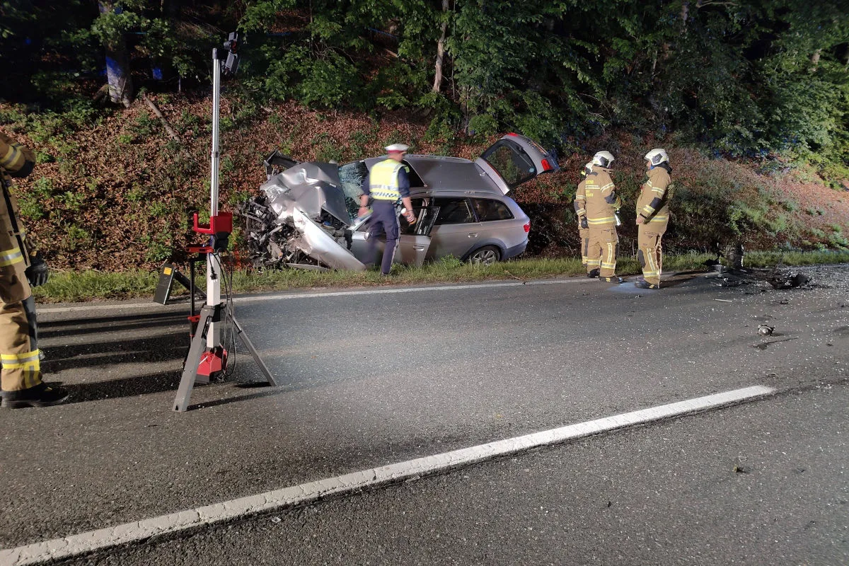 Ein beschädigter silberner Kombi ist in die Böschung gefahren, umgeben von Feuerwehrleuten in Schutzkleidung auf einer nächtlichen Straße.