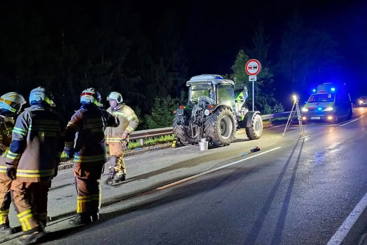 Ein Traktor steht nachts auf einer Straße. Feuerwehrleute sind vor Ort, und ein Polizeifahrzeug ist mit Blaulicht im Hintergrund zu sehen.
