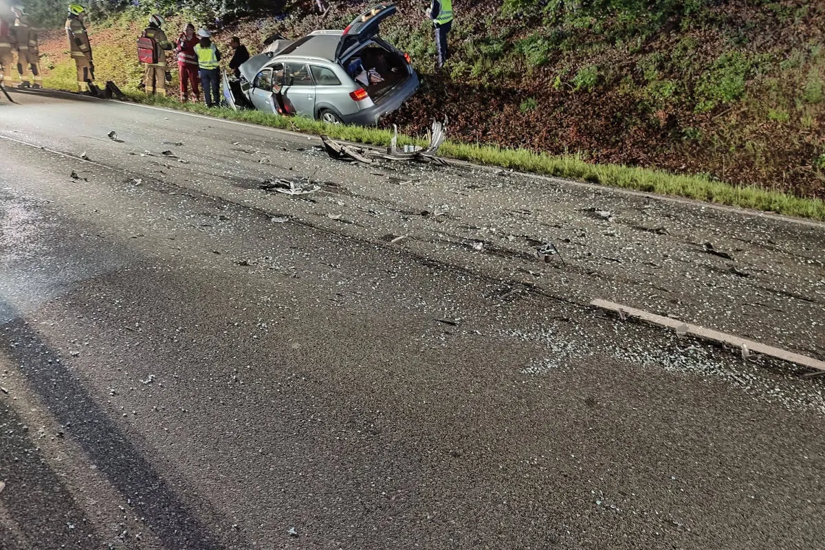 Das Bild zeigt ein Auto, das im Straßengraben einer Autobahn liegt, während Trümmer über die Fahrbahn verteilt sind. Einsatzkräfte stehen neben dem Fahrzeug, dessen Kofferraum geöffnet ist.