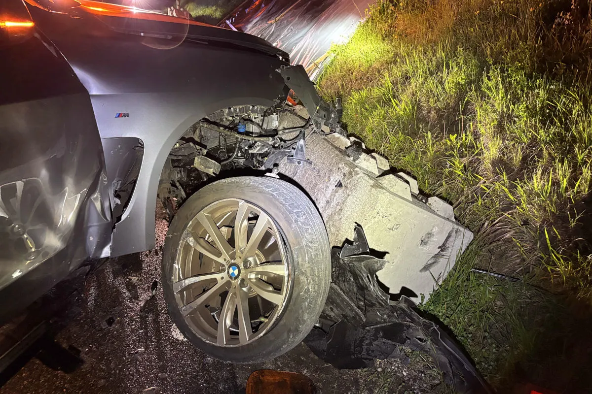 Ein schwer beschädigter BMW steht bei Nacht am Straßenrand. Das Vorderrad ist stark eingeknickt, und die Umgebung ist dunkel und nass.