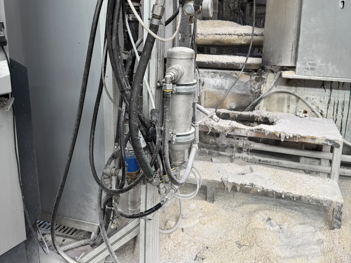 Eine industrielle Maschine mit mehreren Schläuchen und metallischen Rohren. Der Boden ist mit einer Art Pulver bedeckt, das auf einen Vorfall hindeutet.