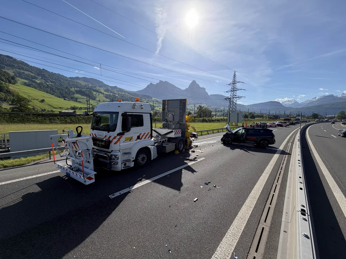 Ein LKW und ein PKW sind auf einer Autobahn in der Schweiz bei klarem Wetter kollidiert. Der LKW hat Absperrungen an Bord, und die Fahrzeuge stehen quer zur Fahrbahn.