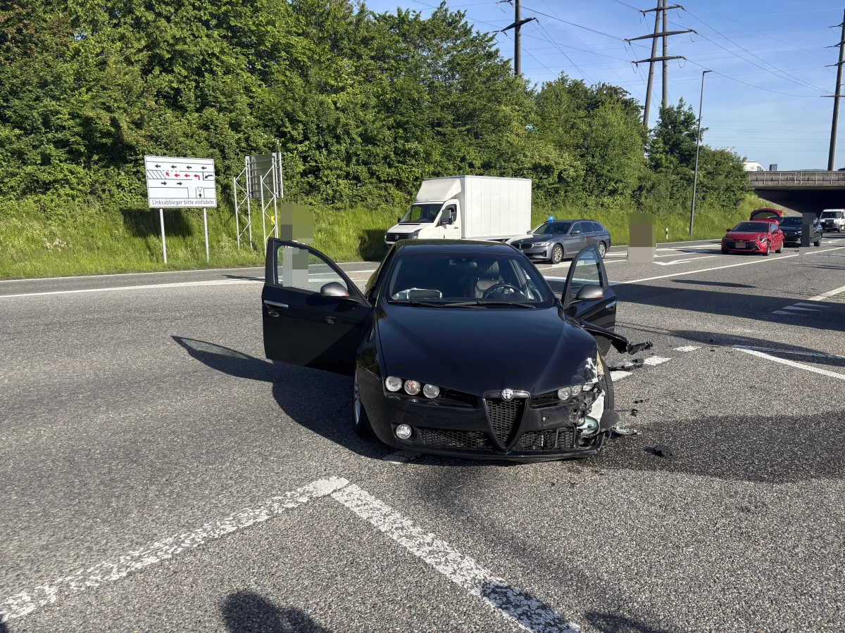 Ein schwarzes Auto mit geöffneten Türen und Frontschaden steht auf einer mehrspurigen Straße. Weitere Fahrzeuge sind im Hintergrund sichtbar.