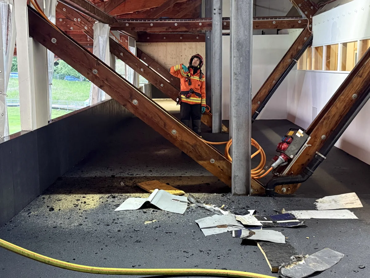 Ein Feuerwehrmann in orangener Schutzkleidung steht in einem Gebäude und untersucht einen Bereich mit herumliegenden Trümmern und beschädigten Strukturen.