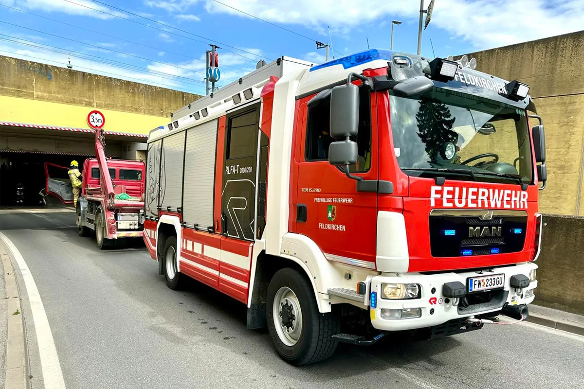 Ein rotes Feuerwehrfahrzeug der Freiwilligen Feuerwehr Feldkirchen ist vor einem Tunnel positioniert. Ein Abschleppwagen holt ein Fahrzeug aus dem Tunnel heraus.