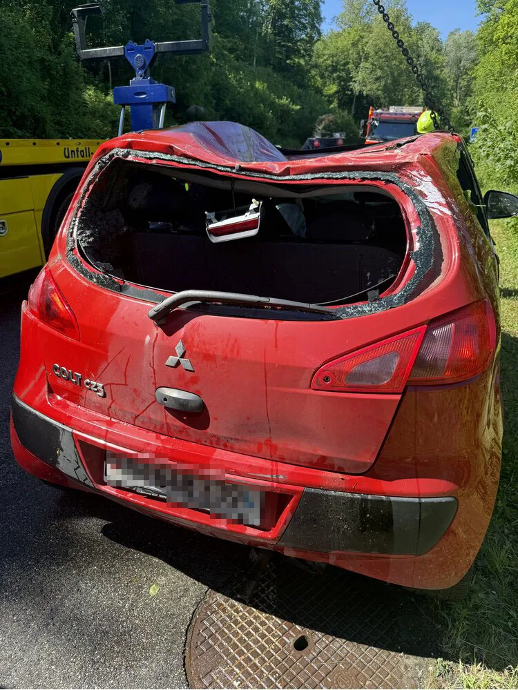 Ein roter Mitsubishi Colt mit stark eingedrücktem Dach wird von einem Kran angehoben. Im Hintergrund ist ein Abschleppfahrzeug zu sehen.