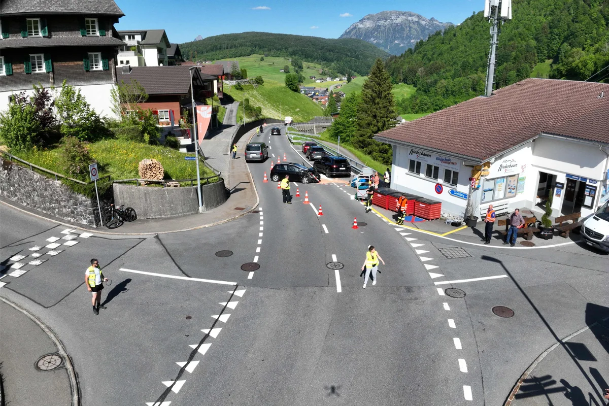 Eine Straße mit Absperrungen und einem Fahrzeug im Vordergrund. Personen in Sicherheitswesten sind anwesend.