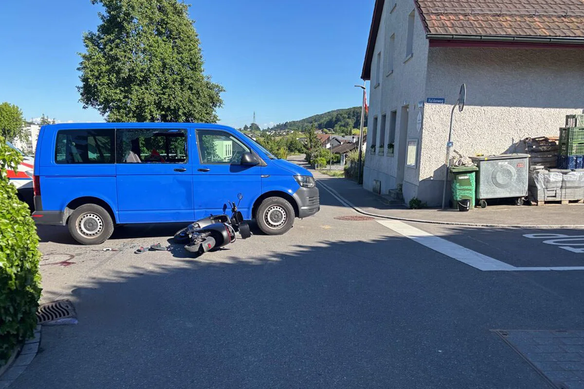 Ein blauer Transporter steht auf einer Straße neben einem gestürzten Roller in einem Wohngebiet. Der Unfall ereignete sich bei Tageslicht.