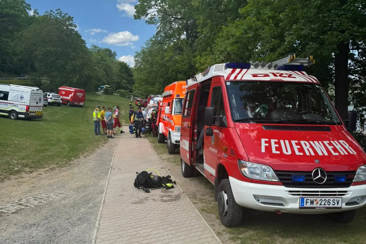 Mehrere rote und weiße Einsatzfahrzeuge von Feuerwehr und Rettung sind auf einem Waldweg geparkt. Einsatzkräfte sind vor Ort und besprechen sich.