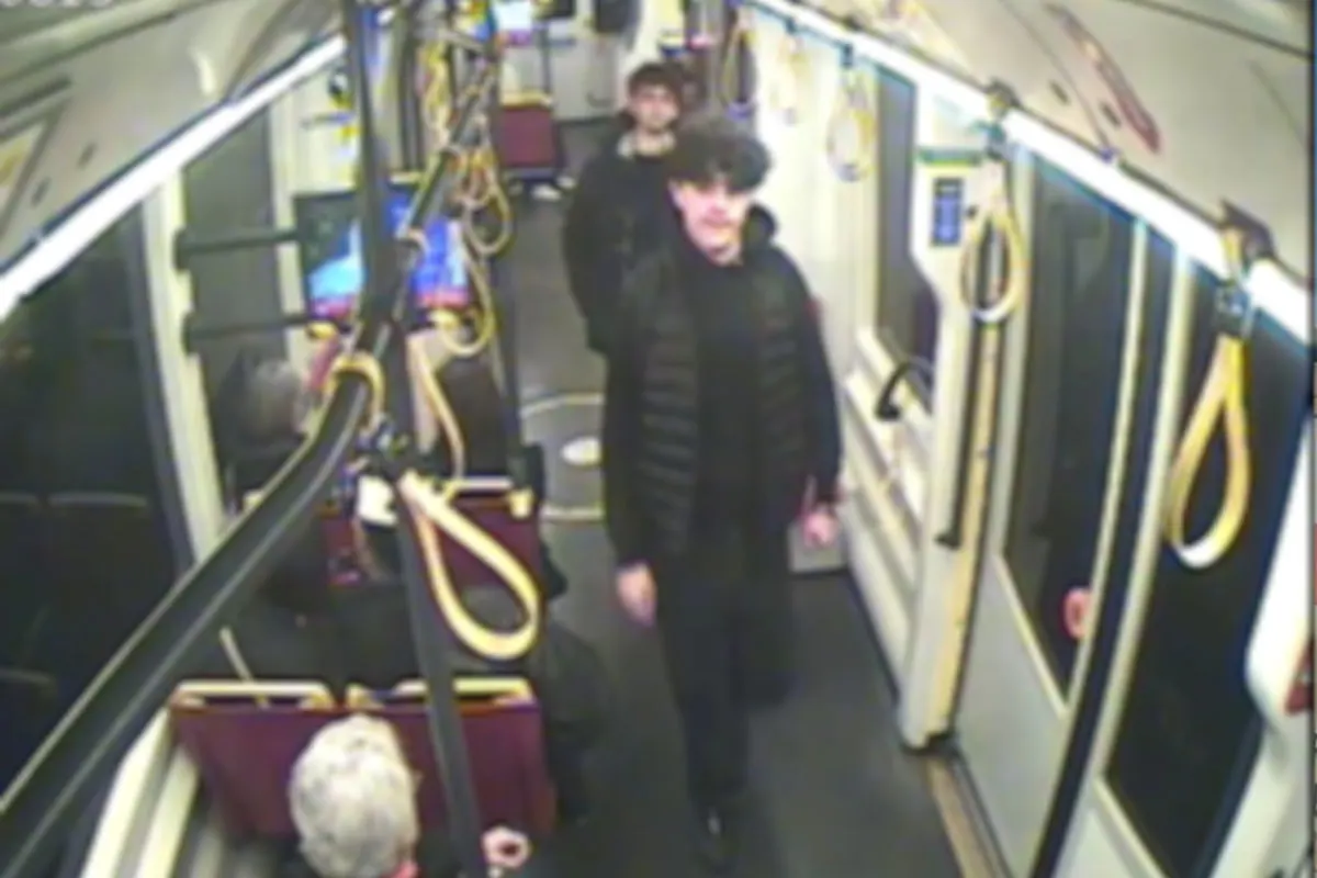 Ein Bild von einer Überwachungskamera in einer Straßenbahn zeigt zwei Personen. Die Innenansicht zeigt Sitzplätze und an den Haltestellen angebrachte Halteschlaufen.