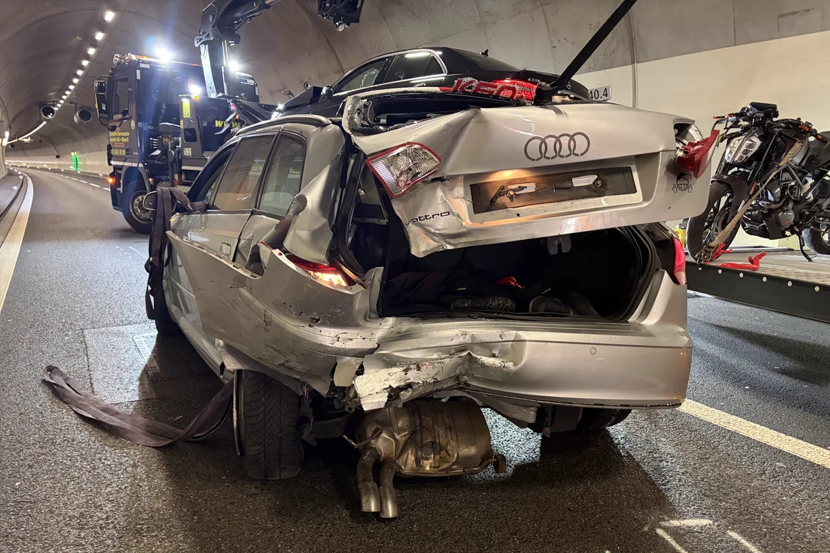 Ein stark beschädigter silberner Audi steht in einem beleuchteten Tunnel. Ein Abschleppwagen ist sichtbar im Hintergrund.