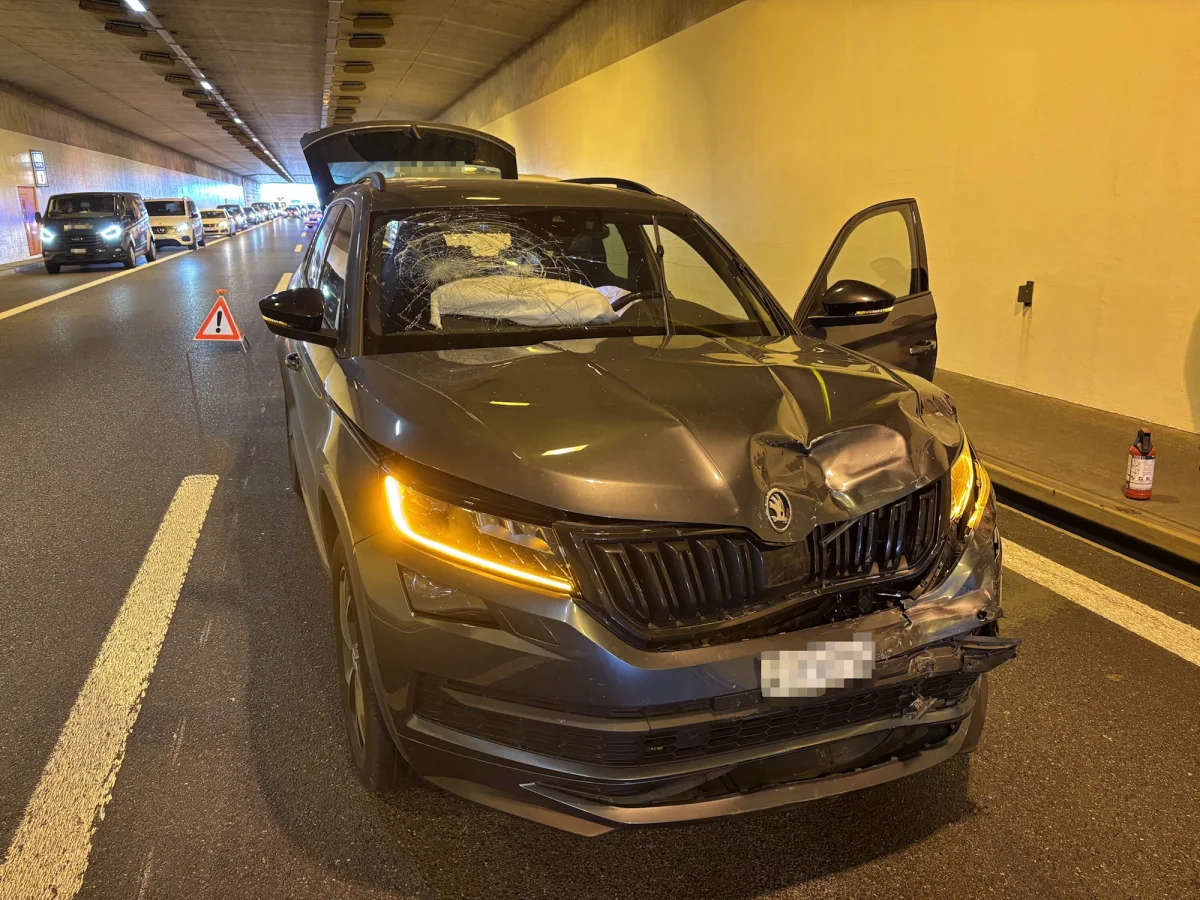 Ein stark beschädigtes Auto steht in einem Tunnel. Die Front und die Windschutzscheibe sind beschädigt, und ein Warndreieck steht davor.
