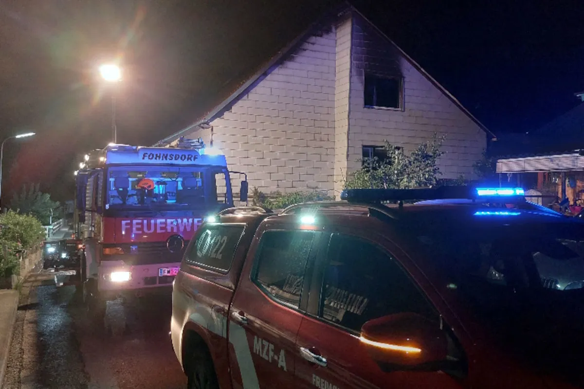 Ein Feuerwehrfahrzeug mit der Aufschrift 'Fohnsdorf' steht bei Nacht vor einem Gebäude. Ein zweites Einsatzfahrzeug ist ebenfalls sichtbar.