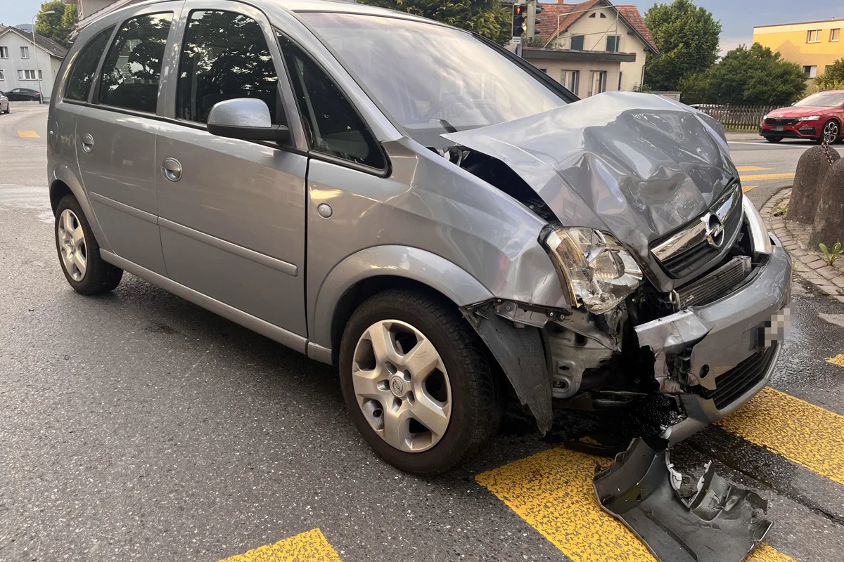 Ein silberner Opel mit stark beschädigter Front steht an einer Straßenkreuzung. Die Frontstoßstange ist verbogen und abgerissen.