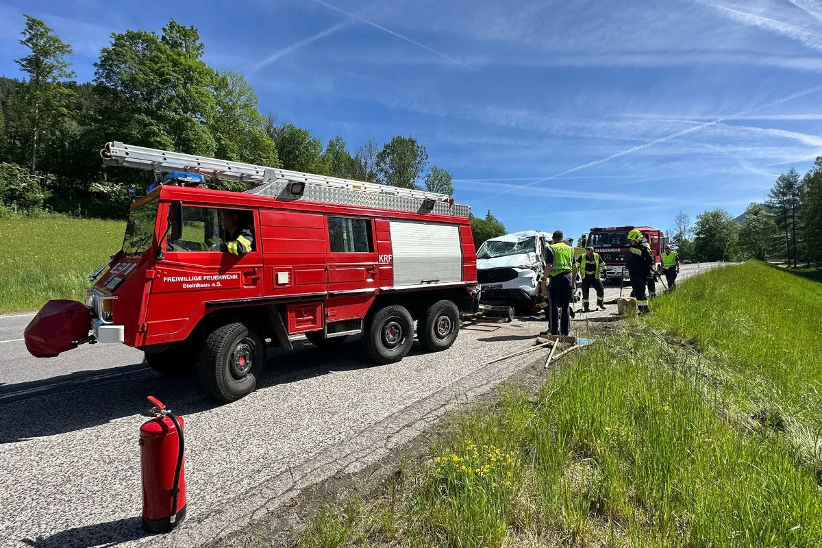Ein rotes Feuerwehrfahrzeug steht neben einem beschädigten weißen Transporter auf einer Landstraße. Feuerwehrleute sind vor Ort tätig.