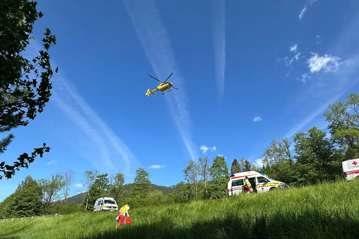 Ein gelber Rettungshelikopter ist am Himmel zu sehen, während unten auf einer Wiese mehrere Rettungsfahrzeuge und Einsatzkräfte arbeiten.
