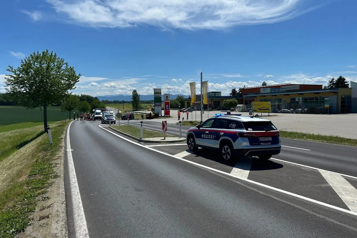 Mehrere Polizeifahrzeuge stehen auf einer Landstraße nahe einer Tankstelle unter blauem Himmel. Polizisten sichern die Unfallstelle ab.