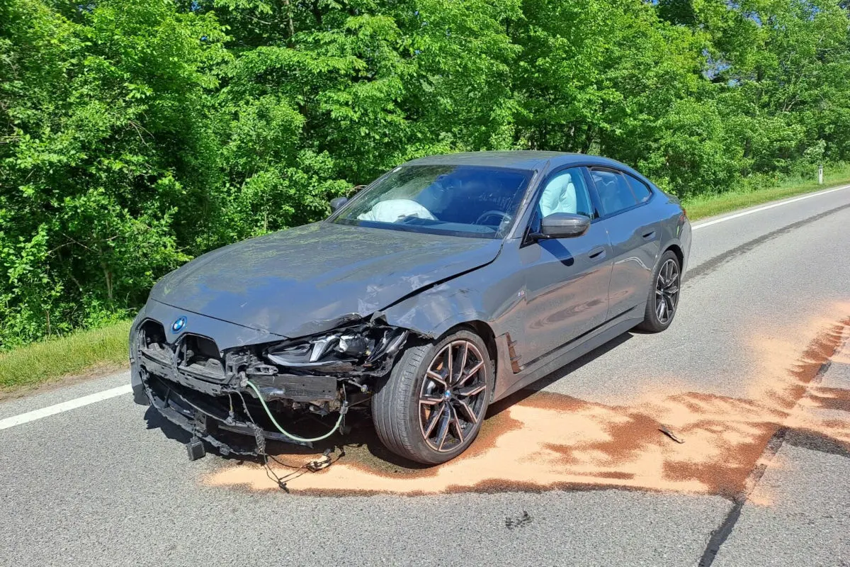 Ein BMW mit erheblichen Frontschäden steht auf einer asphaltierten Landstraße. Der Airbag ist ausgelöst, und es liegt Streugut um das Fahrzeug.