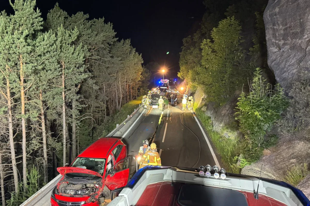 Ein rotes Auto steht beschädigt an einer Waldstraße, während Einsatzkräfte die Unfallstelle nachts absichern.