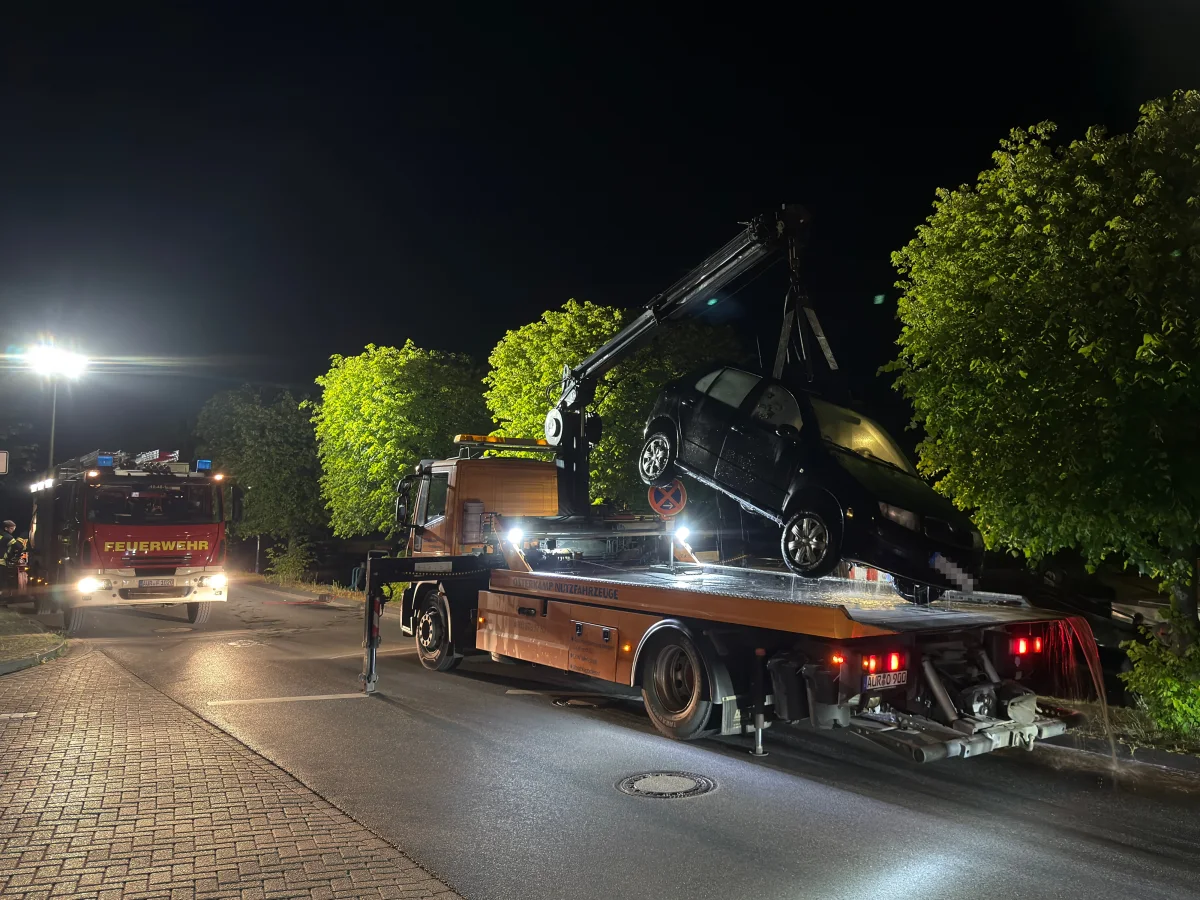 Ein schwarzes Auto wird bei Nacht auf einen Abschleppwagen verladen. Im Hintergrund steht ein Feuerwehrfahrzeug.
