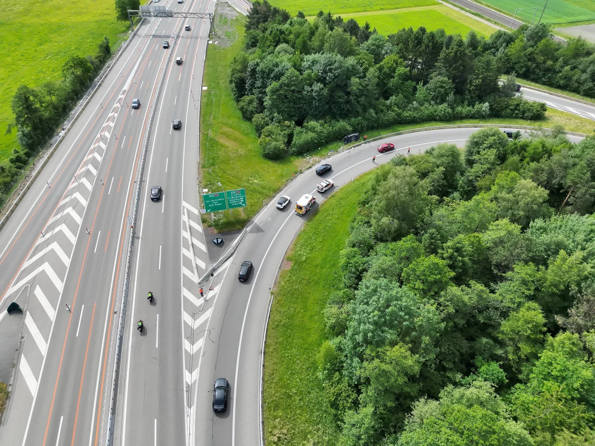 Luftaufnahme einer Autobahn mit mehreren Fahrzeugen auf unterschiedlichen Fahrspuren. Ein Polizeifahrzeug ist in einer Kurve sichtbar.