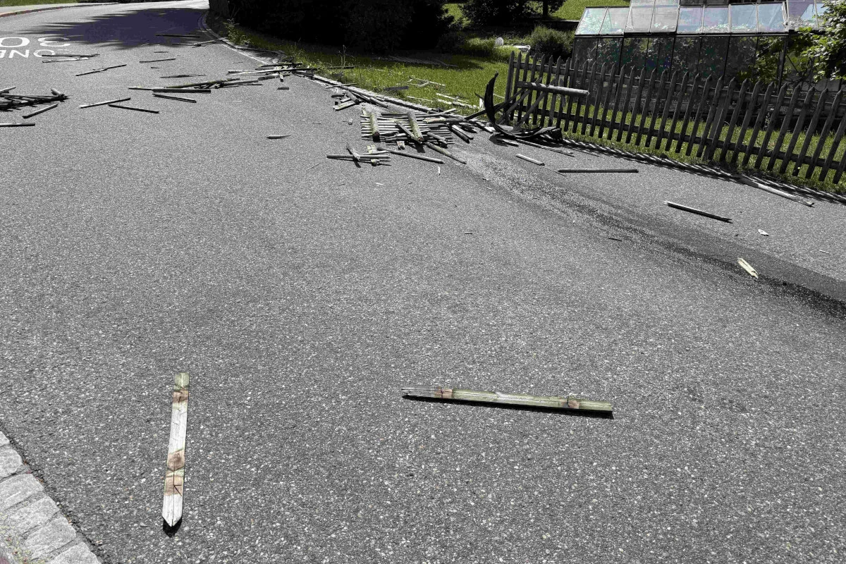 Die Straße zeigt verstreute Trümmer und einen beschädigten Gartenzaun nahe einer Kurve.