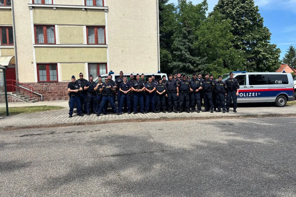 Eine Gruppe von Polizisten posiert in einer Reihe vor einem großen, mit 'Polizei' beschrifteten Transporter. Es ist ein sonniger Tag.