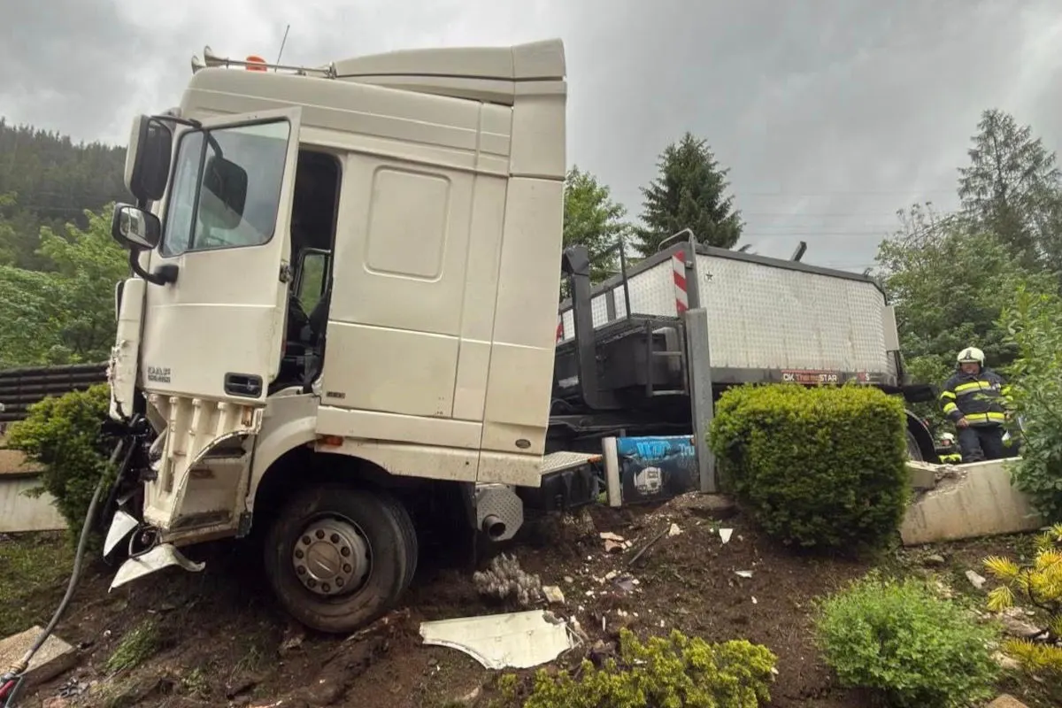 Ein schwerer Lkw ist von der Straße abgekommen und steckt an einem Abhang fest. Ein Feuerwehrmann in Uniform steht in der Nähe.