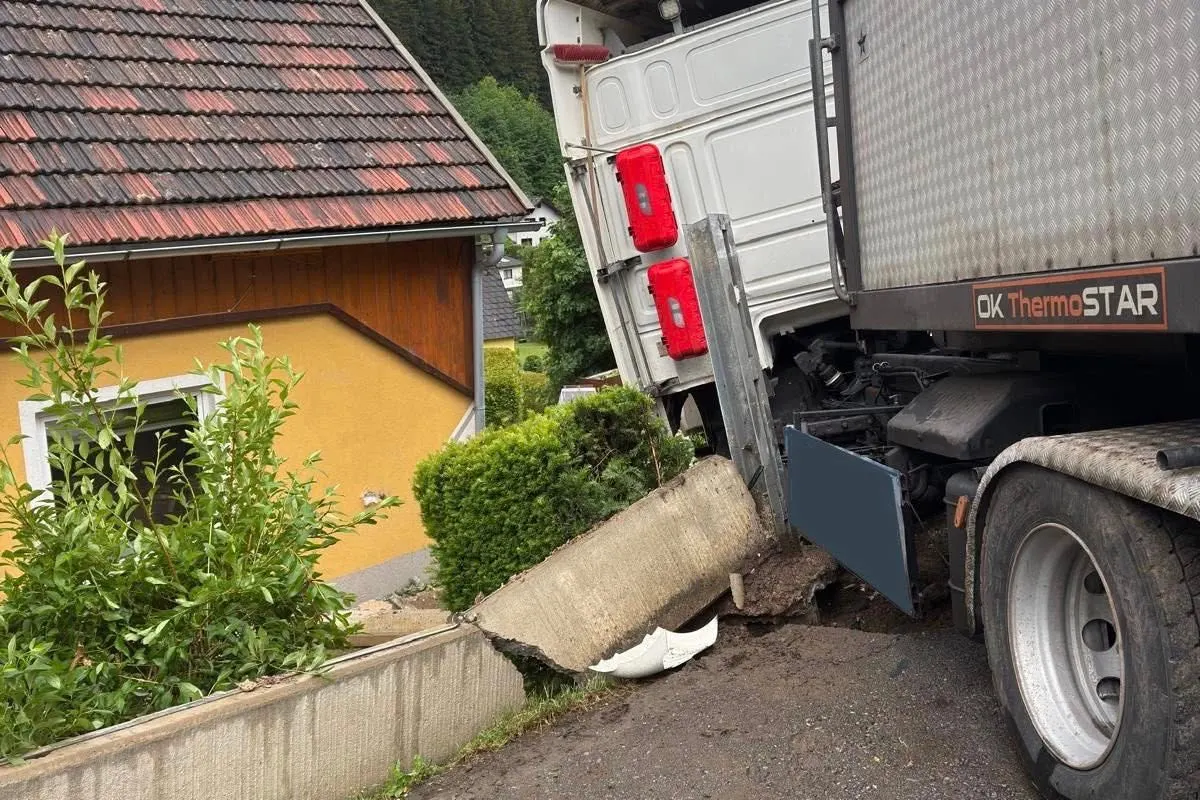 Ein Lastwagen ist rückwärts gegen ein gelbes Haus gefahren, wobei die Fassade beschädigt wurde. Teile des Gartens sind ebenfalls betroffen.