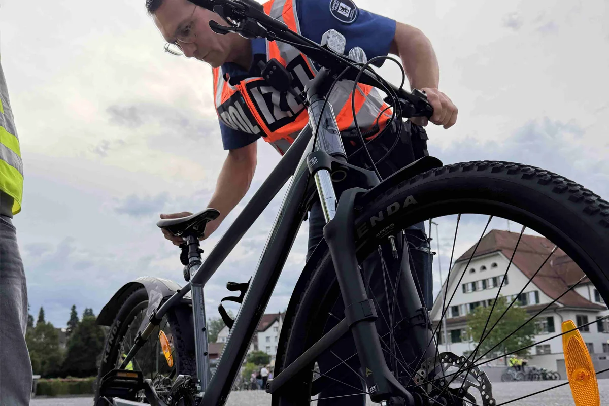Ein Polizist in Uniform mit einer leuchtenden Weste inspiziert ein Fahrrad vor einem Gebäude bei bewölktem Himmel.