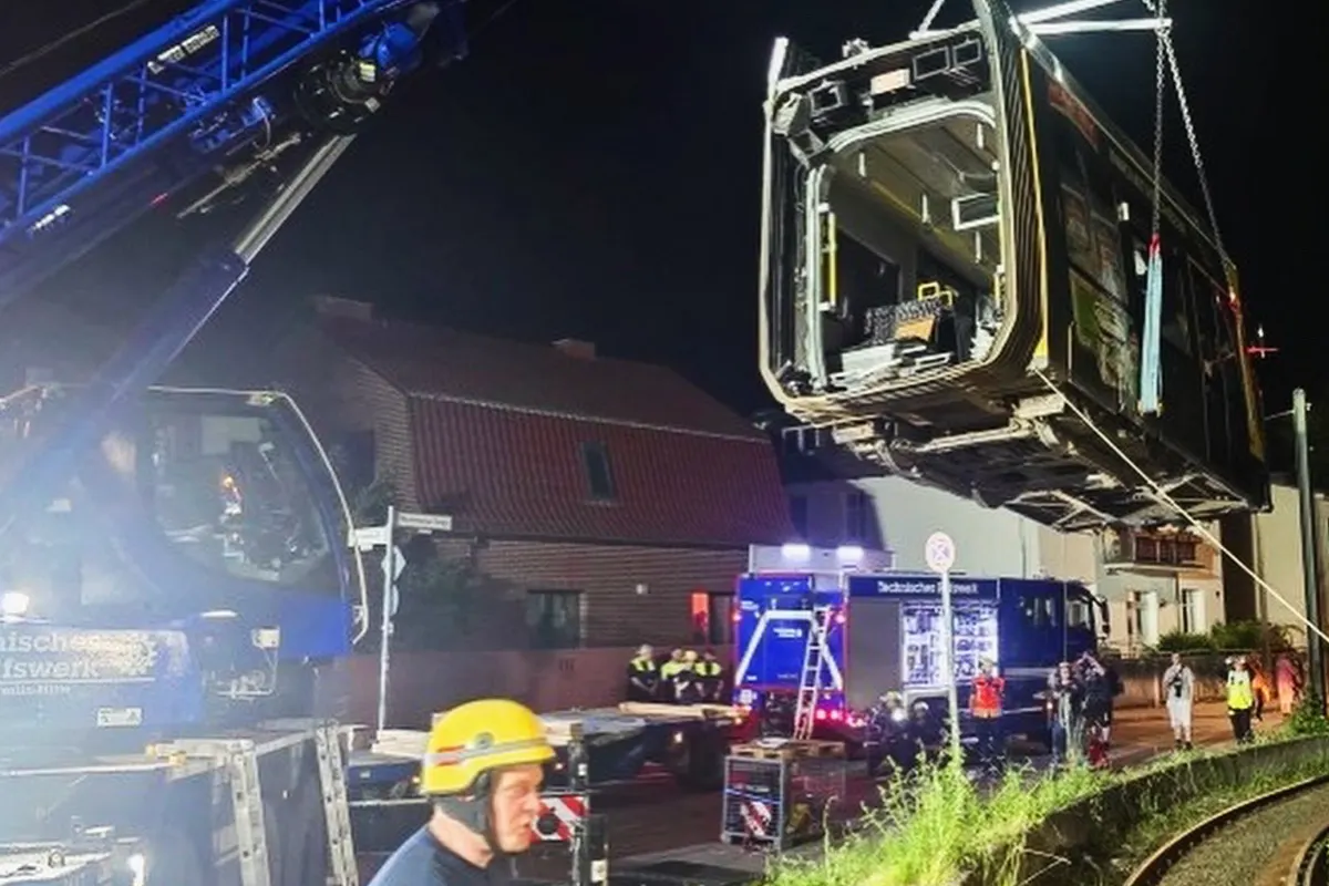 Bei Nacht hebt ein Kran eine beschädigte Straßenbahn an. Mehrere Personen, teils in Einsatzkleidung, sind vor Ort aktiv.