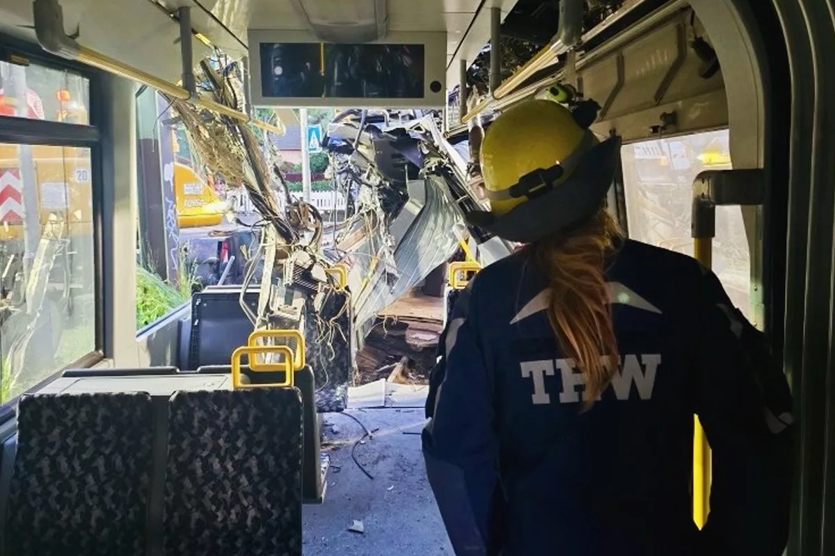 Ein THW-Mitarbeiter in Schutzkleidung steht in einem Bus, dessen Innenraum durch einen Unfall stark beschädigt wurde. Der vordere Bereich des Busses zeigt freigelegte Kabel und Trümmerteile.