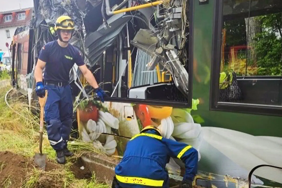 Zwei Einsatzkräfte in Schutzkleidung arbeiten an einer stark beschädigten Straßenbahn. Die Front der Bahn ist eingedrückt.