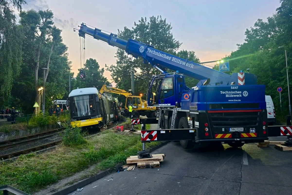 Ein Kran des Technischen Hilfswerks hebt eine auf den Schienen entgleiste Straßenbahn an. Arbeiter sind am Einsatzort im Stadtgebiet sichtbar, während eine Absperrung die Straße blockiert.