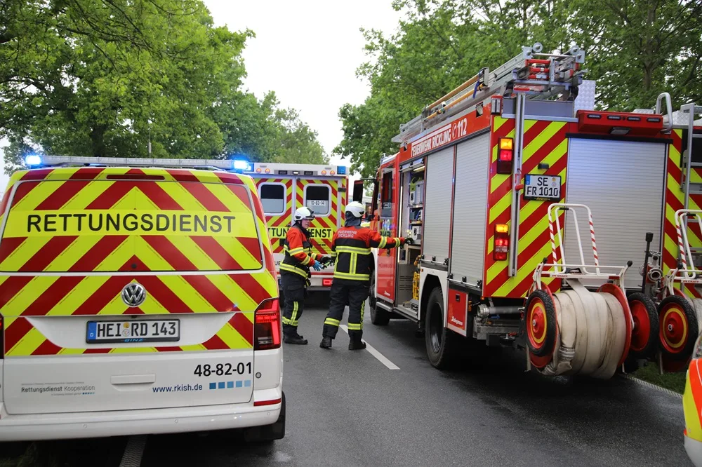 Ein Rettungsfahrzeug des Rettungsdienstes und ein Feuerwehrfahrzeug stehen auf einer Landstraße im Einsatz. Mehrere Einsatzkräfte sind vor Ort.