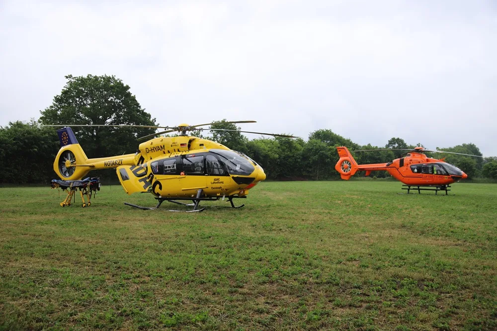 Zwei Rettungshubschrauber stehen nebeneinander auf einer Wiese. Der vordere ist gelb mit dem ADAC-Logo, der hintere orange.