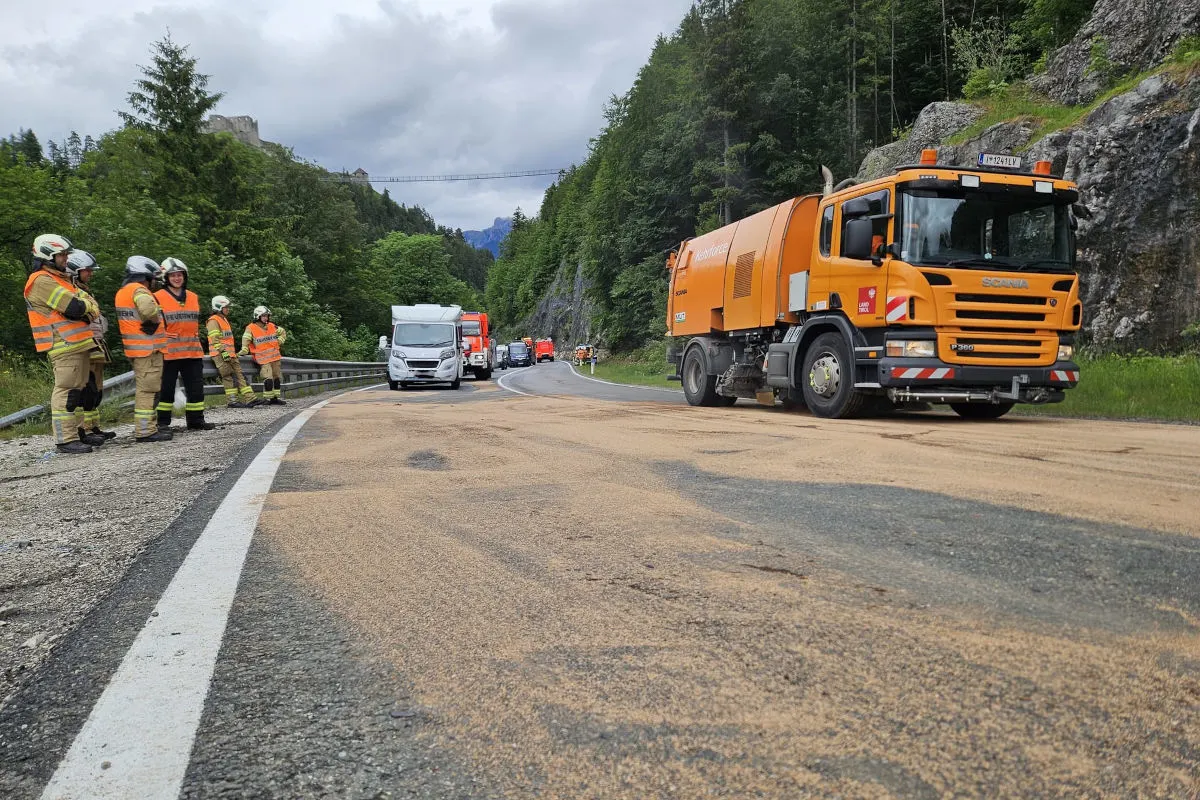 Ein orangefarbener Lastwagen steht auf einer Landstraße. Feuerwehrkräfte in orangefarbenen Westen stehen am Straßenrand.