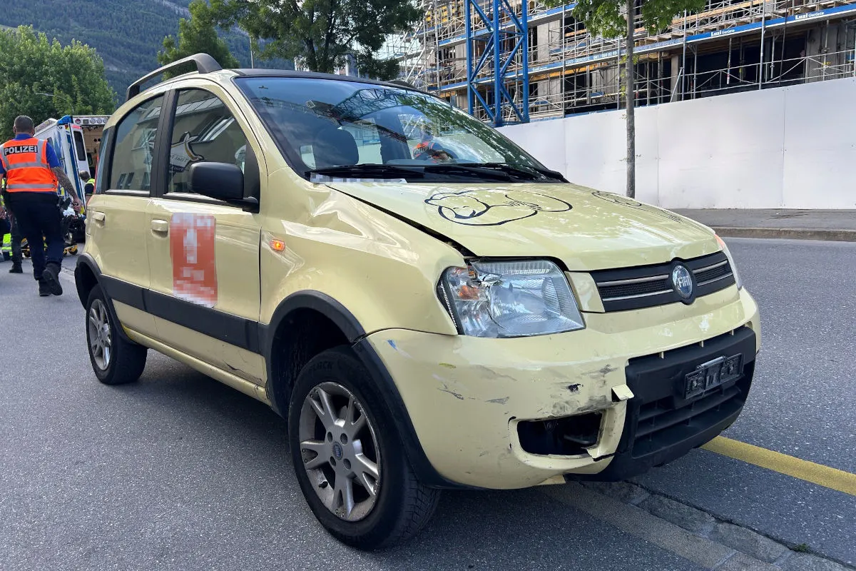 Ein gelber Fiat zeigt deutliche Schäden an Stoßfänger und Motorhaube. Im Hintergrund sind Polizisten und ein Rettungswagen zu sehen.