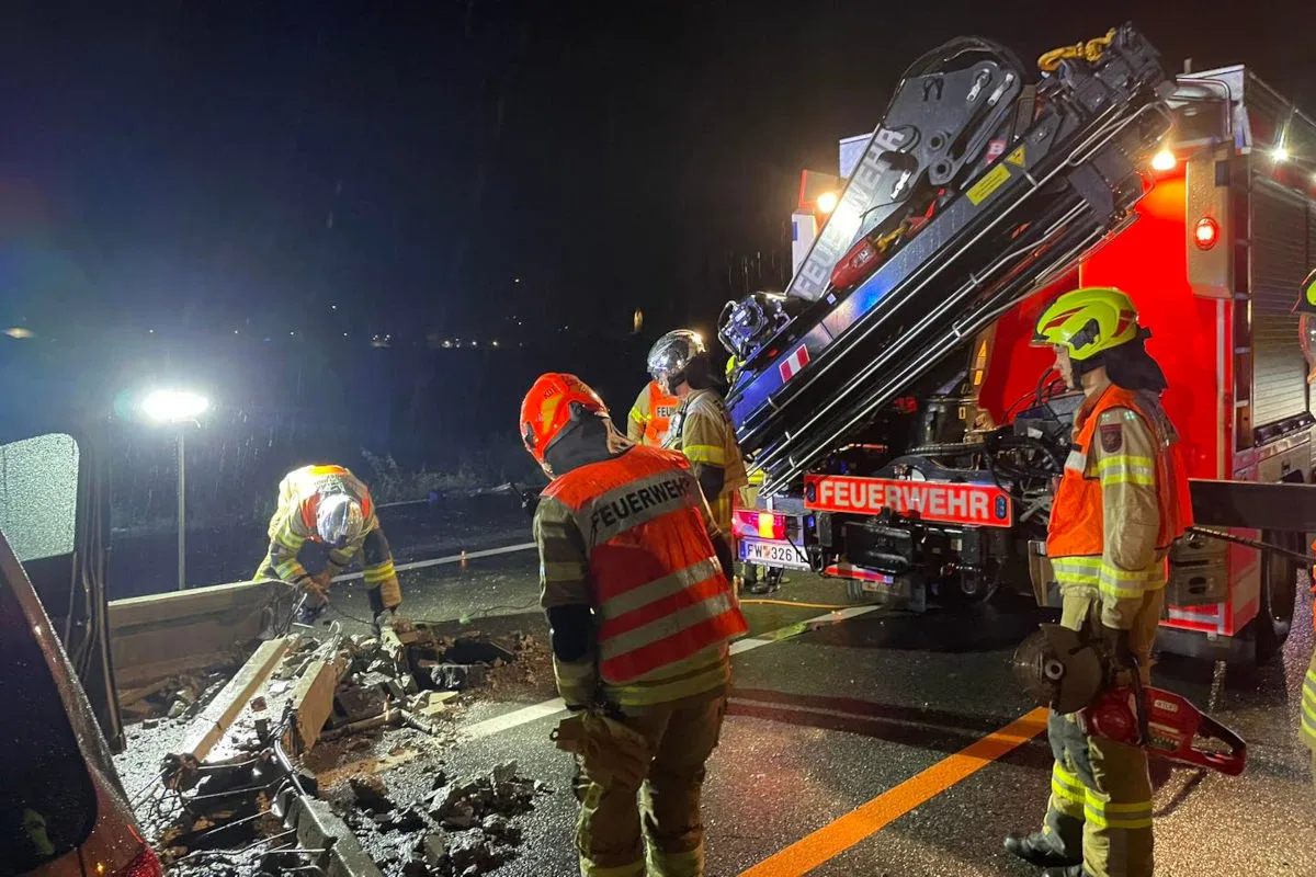 Mehrere Feuerwehrleute stehen nachts neben einem Feuerwehrauto auf einer Autobahn und beseitigen Trümmer an einer beschädigten Leitplanke.