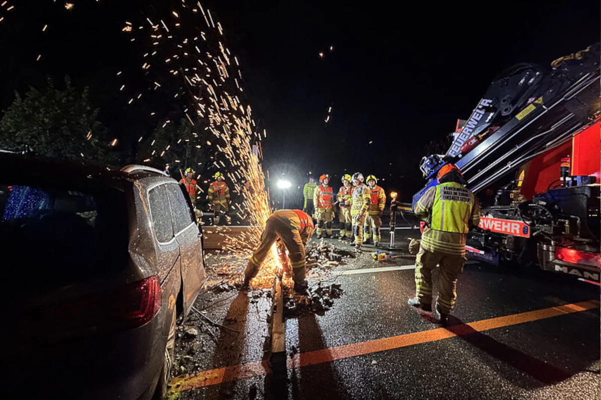 Mehrere Feuerwehrleute sind bei Nacht im Einsatz. Ein Feuerwehrmann arbeitet mit Funkenflug an einem verunfallten Fahrzeug, während andere zusehen.