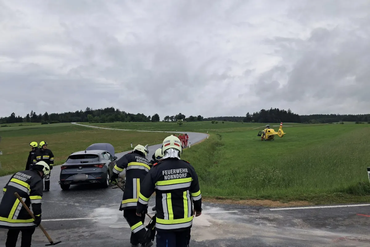 Ein gelber Rettungshubschrauber steht auf einem Feld neben einer Landstraße. Mehrere Feuerwehrleute arbeiten an einem verunglückten Auto.
