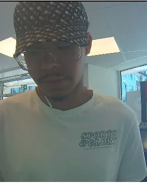 Ein Mann trägt eine Brille und eine gemusterte Mütze in einem Innenraum. Er hat ein T-Shirt mit Aufdruck an.