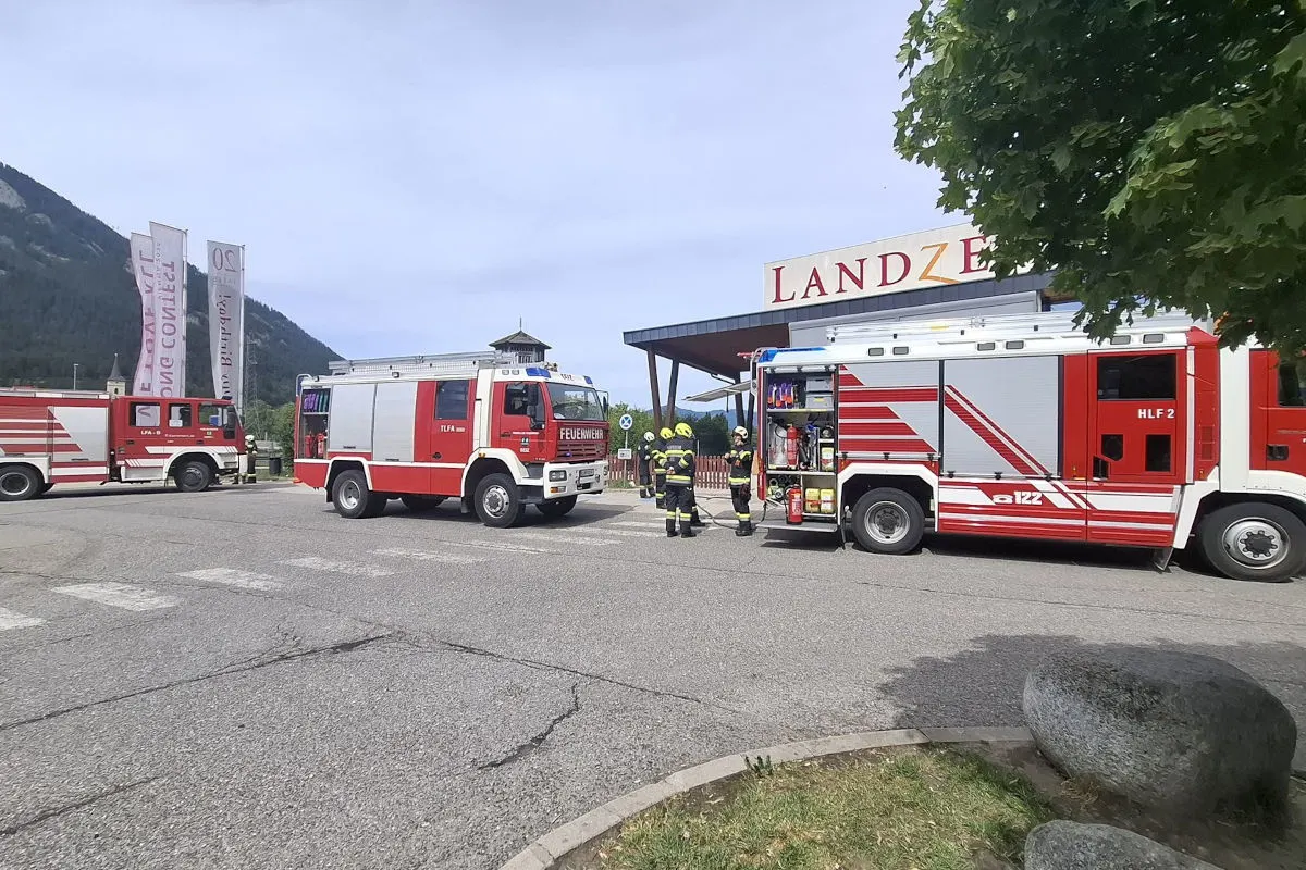 Drei rote Feuerwehrfahrzeuge stehen vor einem Gebäude mit der Aufschrift 'Landzeit'; Feuerwehrleute in Einsatzkleidung sind zu sehen.