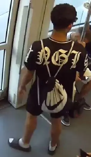 Ein Mann mit dunklem T-Shirt und kurzen Hosen steht in einer Straßenbahn und ist von hinten zu sehen.