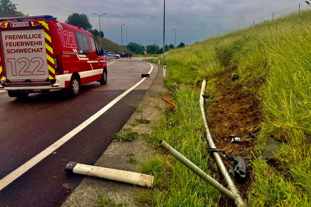 Ein Rettungswagen der Feuerwehr Schwechat steht auf einer Straße, während im Vordergrund eine beschädigte Leitplanke und Spuren im Gras sichtbar sind.
