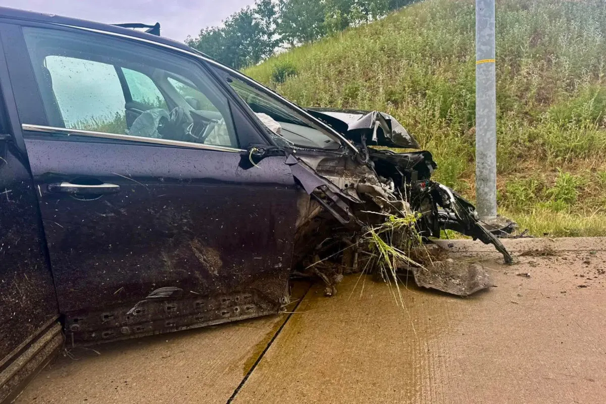 Ein Fahrzeug mit schwer beschädigter Front steht neben einer Straßenlaterne auf einer ländlichen Straße. Gras steht vor der Stoßstange.