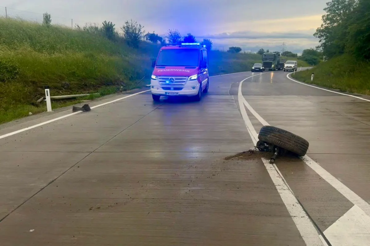 Ein Feuerwehrfahrzeug mit aktiviertem Blaulicht steht auf einer nassen Autobahn. Auf der Fahrbahn liegt ein abgerissenes Rad.